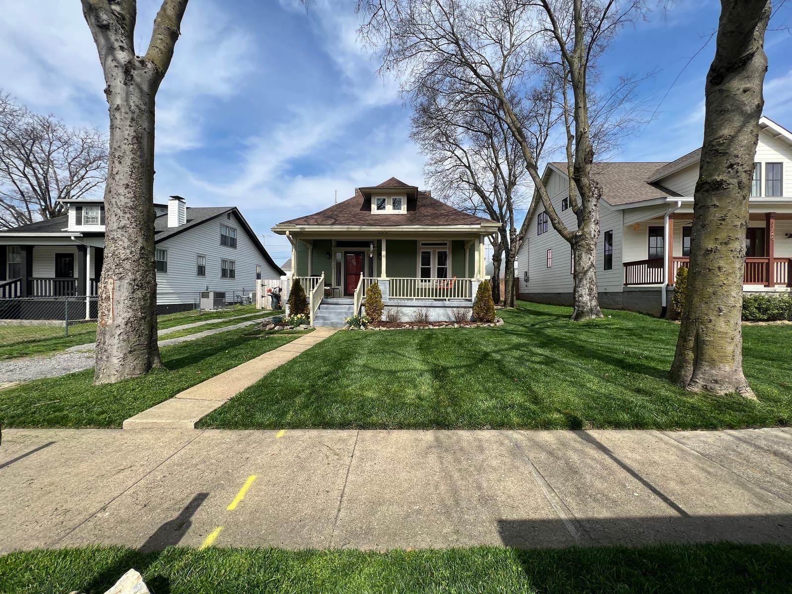 Tidy front yard and walkway in front of a green bungalow with fresh beds along the porch