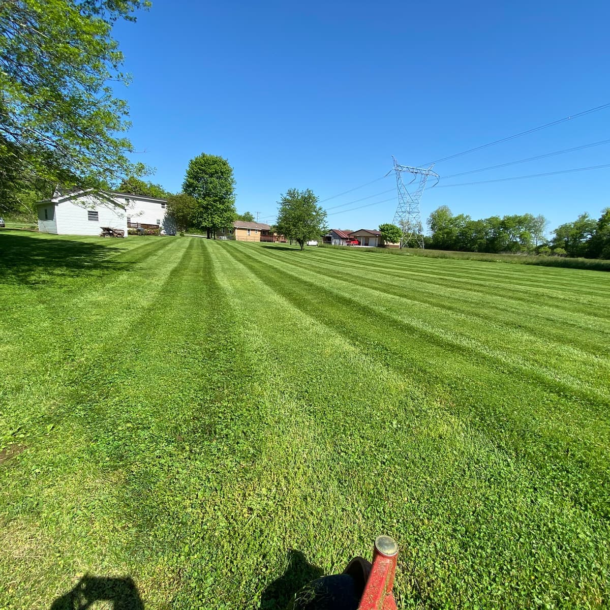 Large open lot mowed in wide, even stripes under a clear blue sky